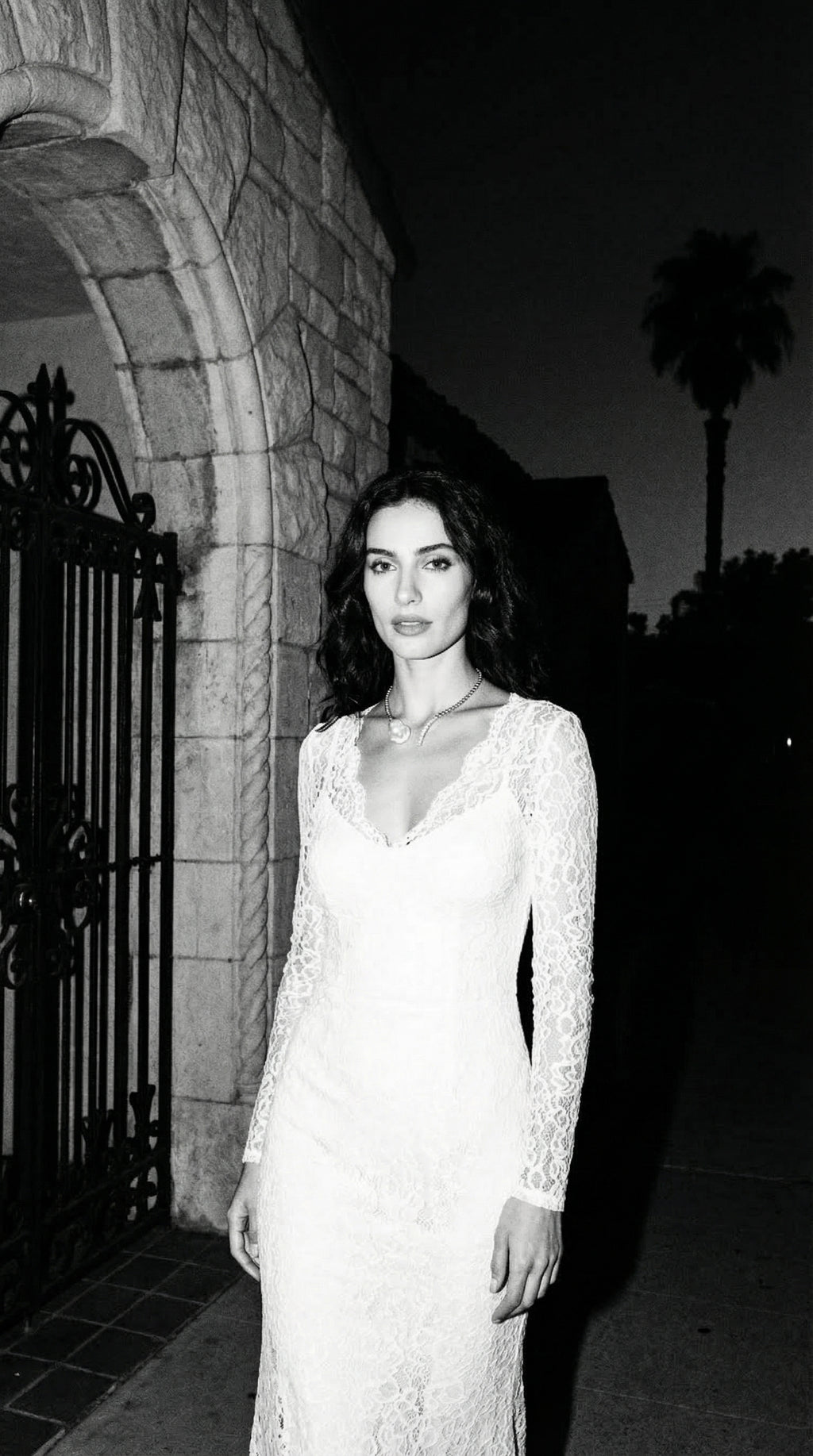 Woman in a long-sleeve dress standing in front of a stone building at night.