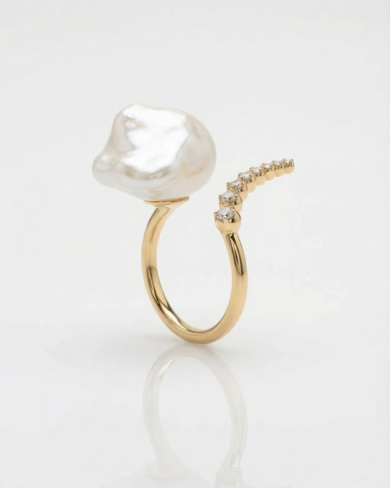 Gold bypass ring with a large pearl and diamonds on a white background